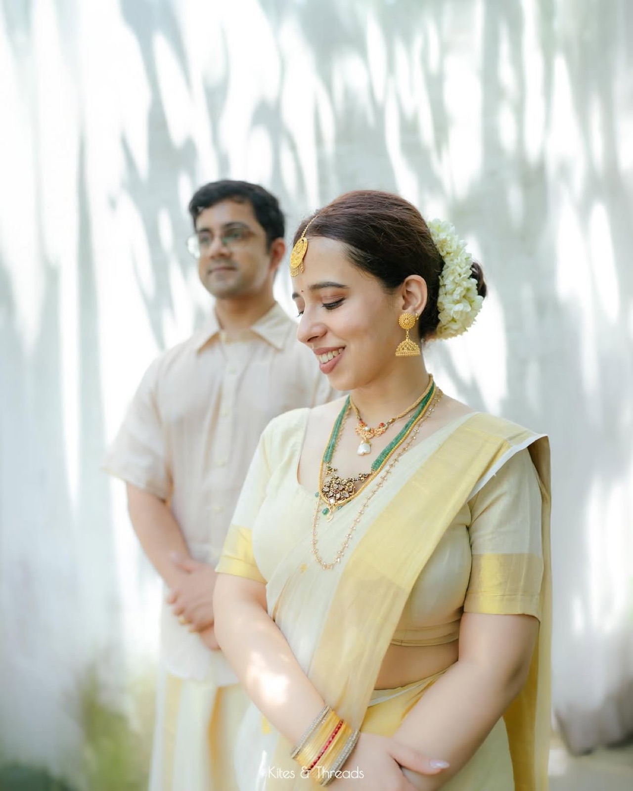 A couple in pale Kerala kasavu attire against dappled light